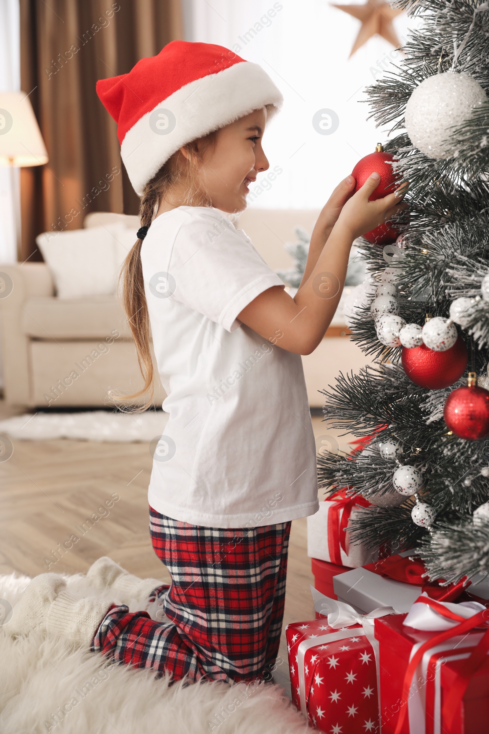 Photo of Cute little girl decorating Christmas tree at home