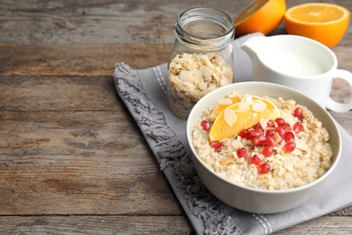 Photo of Bowl of quinoa porridge with nuts, orange and pomegranate seeds served for breakfast on wooden table. Space for text