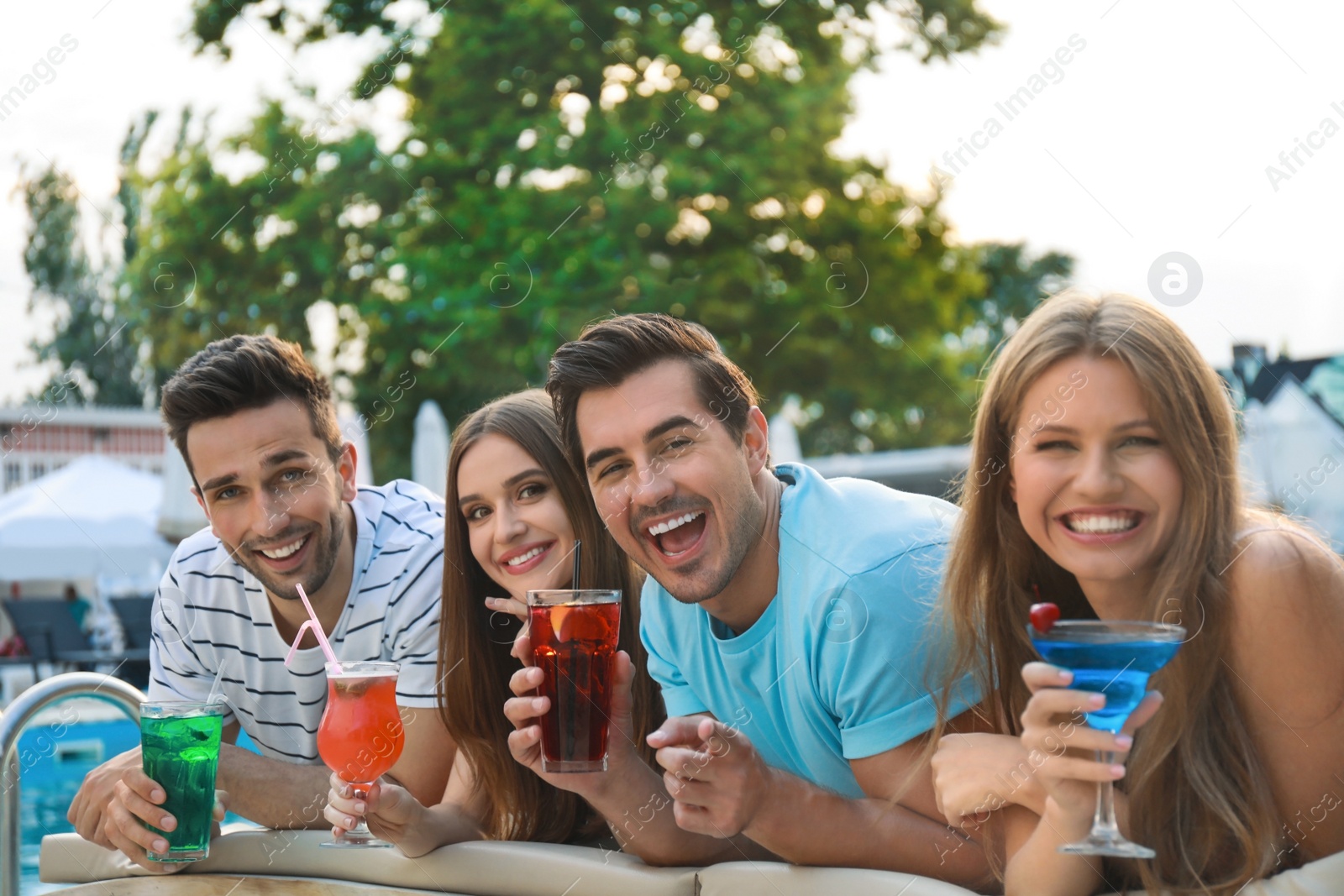 Photo of Happy young friends with fresh summer cocktails relaxing near swimming pool