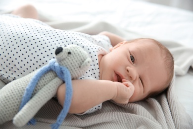 Adorable newborn baby with toy bear lying on soft blanket