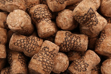 Many corks of wine bottles with grape images as background, top view