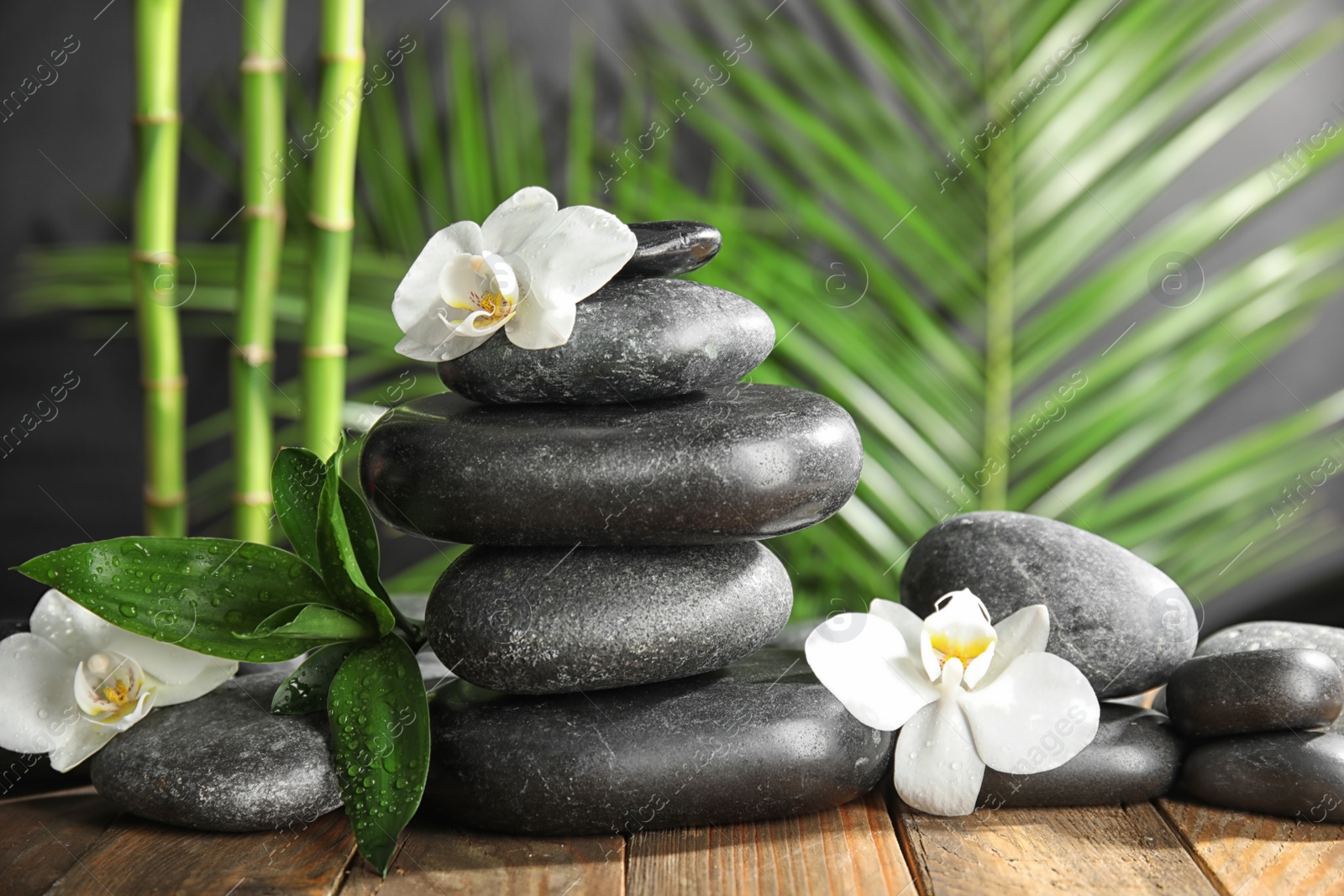 Photo of Spa stones with flowers on wooden table against blurred bamboo branches