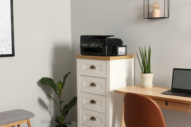 Photo of Modern printer on chest of drawers near wooden table indoors