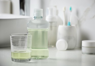 Mouthwash and glass on white countertop in bathroom. Space for text