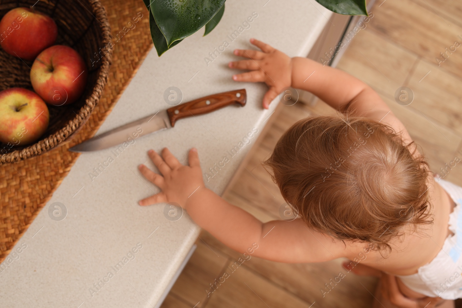 Photo of Little child reaching for knife on light countertop, above view. Dangers in kitchen