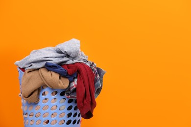 Photo of Laundry basket with clothes against orange background. Space for text