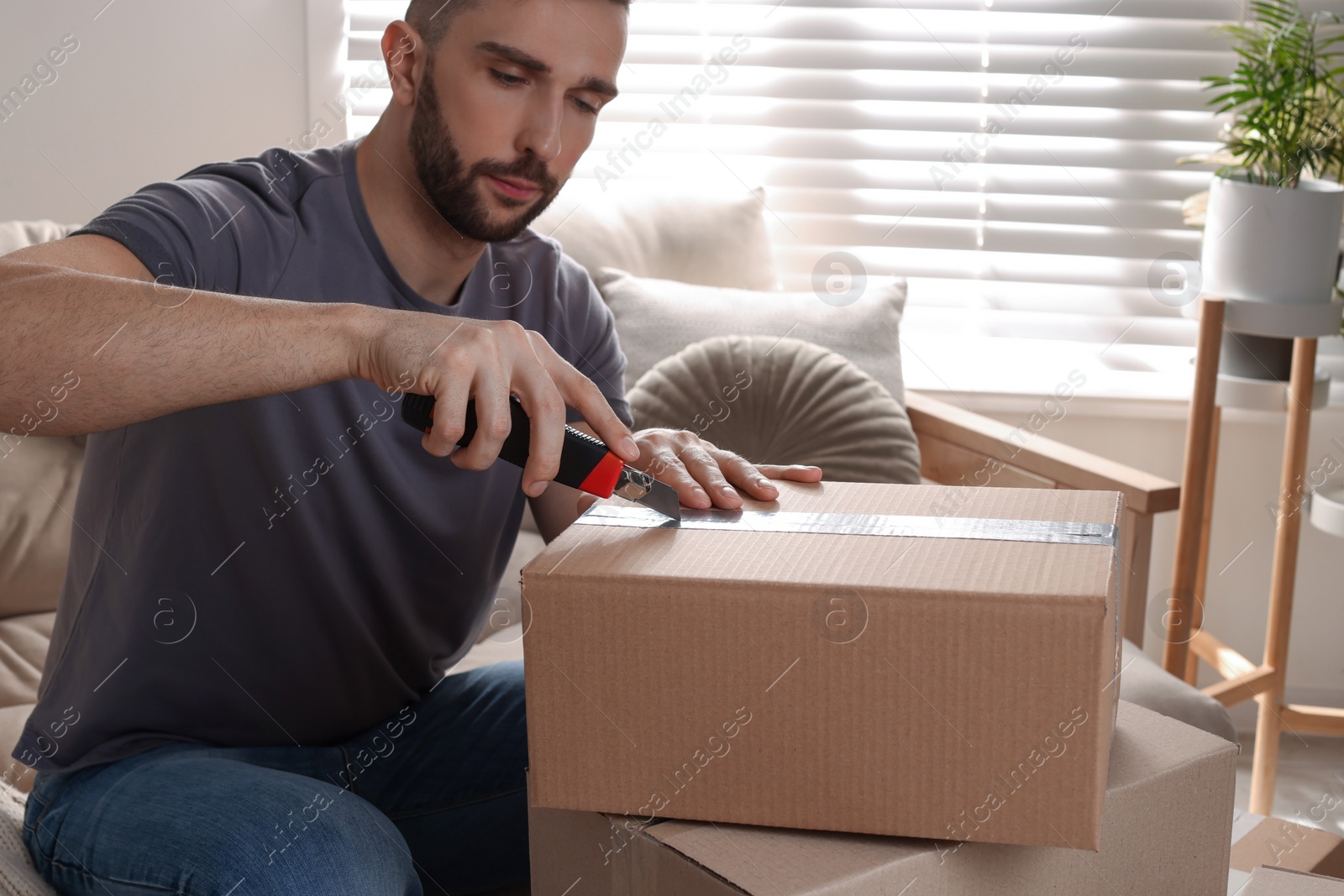 Photo of Man using utility knife to open parcel at home