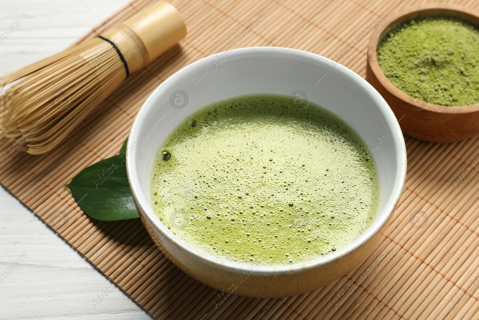Photo of Cup of fresh matcha tea, bamboo whisk and green powder on table, closeup