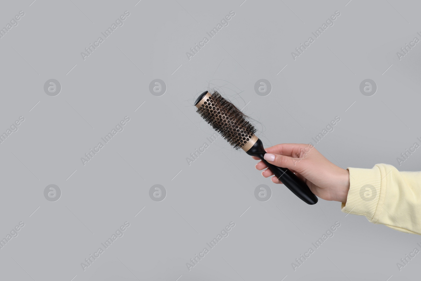 Photo of Woman holding brush with lost hair on grey background, closeup and space for text. Alopecia problem