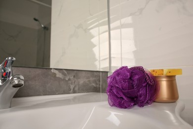Photo of Purple shower puff and cosmetic products on sink in bathroom, space for text