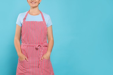 Photo of Woman in clean striped apron on light blue background, closeup. Space for text