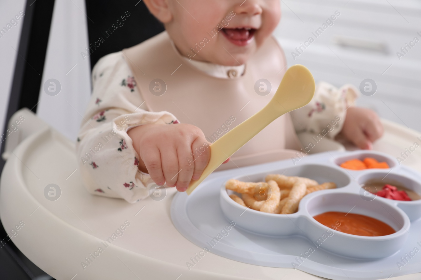 Photo of Little baby eating food in high chair indoors, closeup