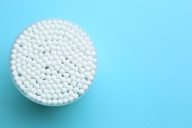 Photo of Many cotton buds in container on light blue background, top view. Space for text