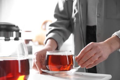 Woman with cup of hot tea at white table, closeup