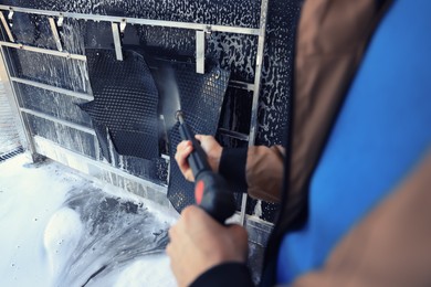 Photo of Man cleaning auto mats with high pressure water jet at self-service car wash, closeup