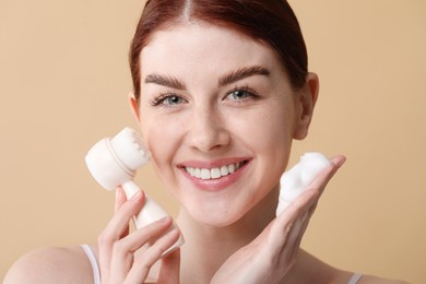 Photo of Washing face. Young woman with brush and cleansing foam on beige background, closeup