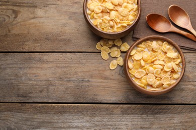 Photo of Tasty cornflakes with milk in bowls on wooden table, flat lay. Space for text