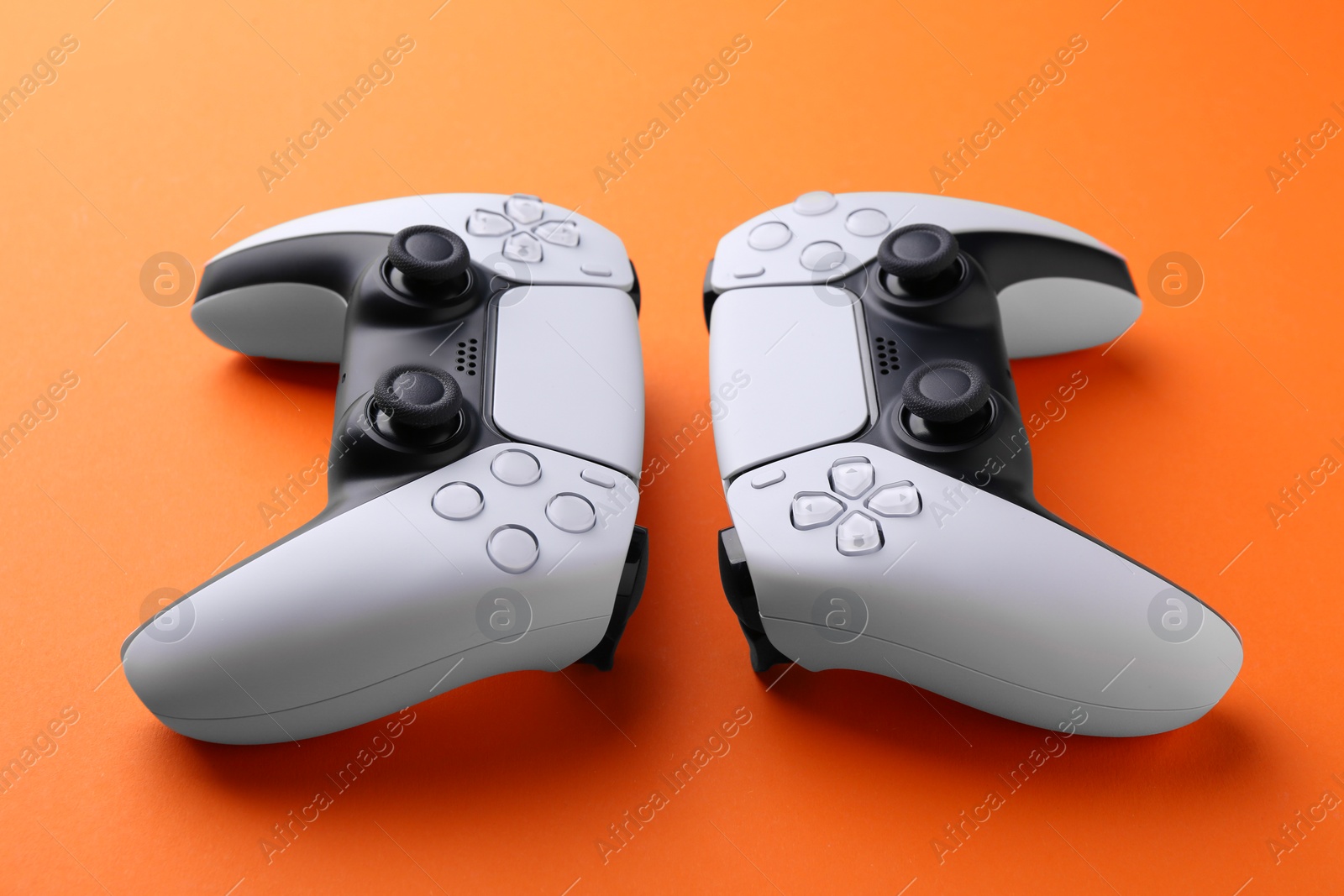 Photo of Two wireless game controllers on orange background