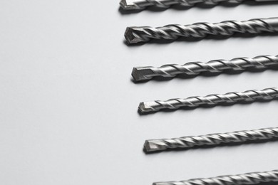 Different drill bits on light background, closeup. Space for text