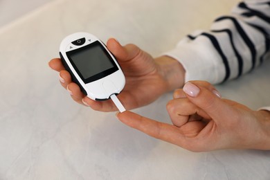 Photo of Diabetes. Woman checking blood sugar level with glucometer at light table, closeup