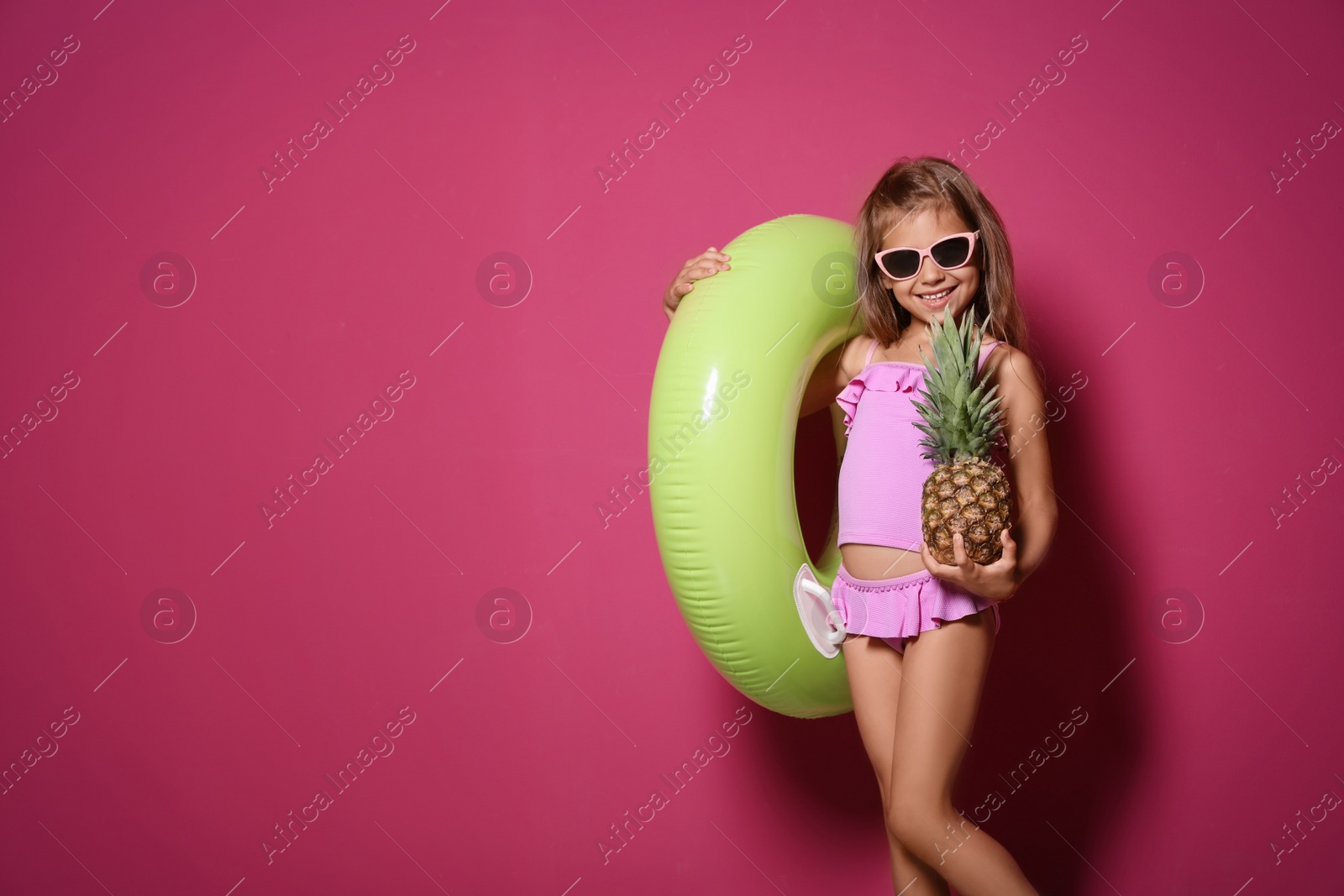 Photo of Cute little girl with pineapple and bright inflatable ring on color background