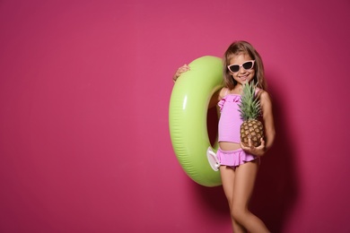 Cute little girl with pineapple and bright inflatable ring on color background