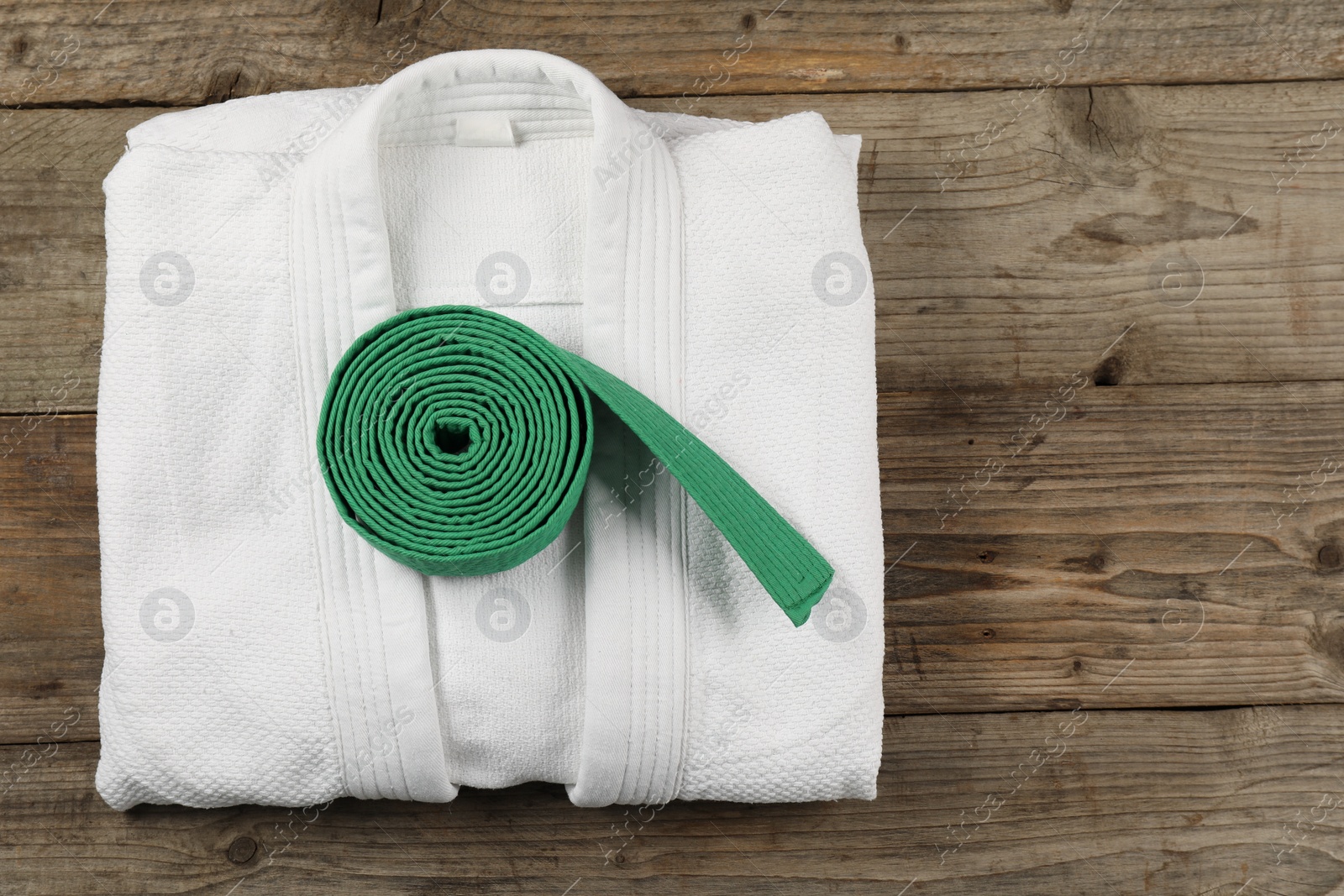 Photo of Green karate belt and white kimono on wooden background, top view. Space for text