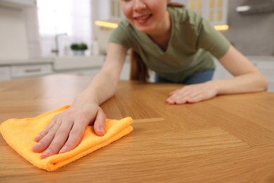 Photo of Woman with microfiber cloth cleaning wooden table in kitchen, closeup