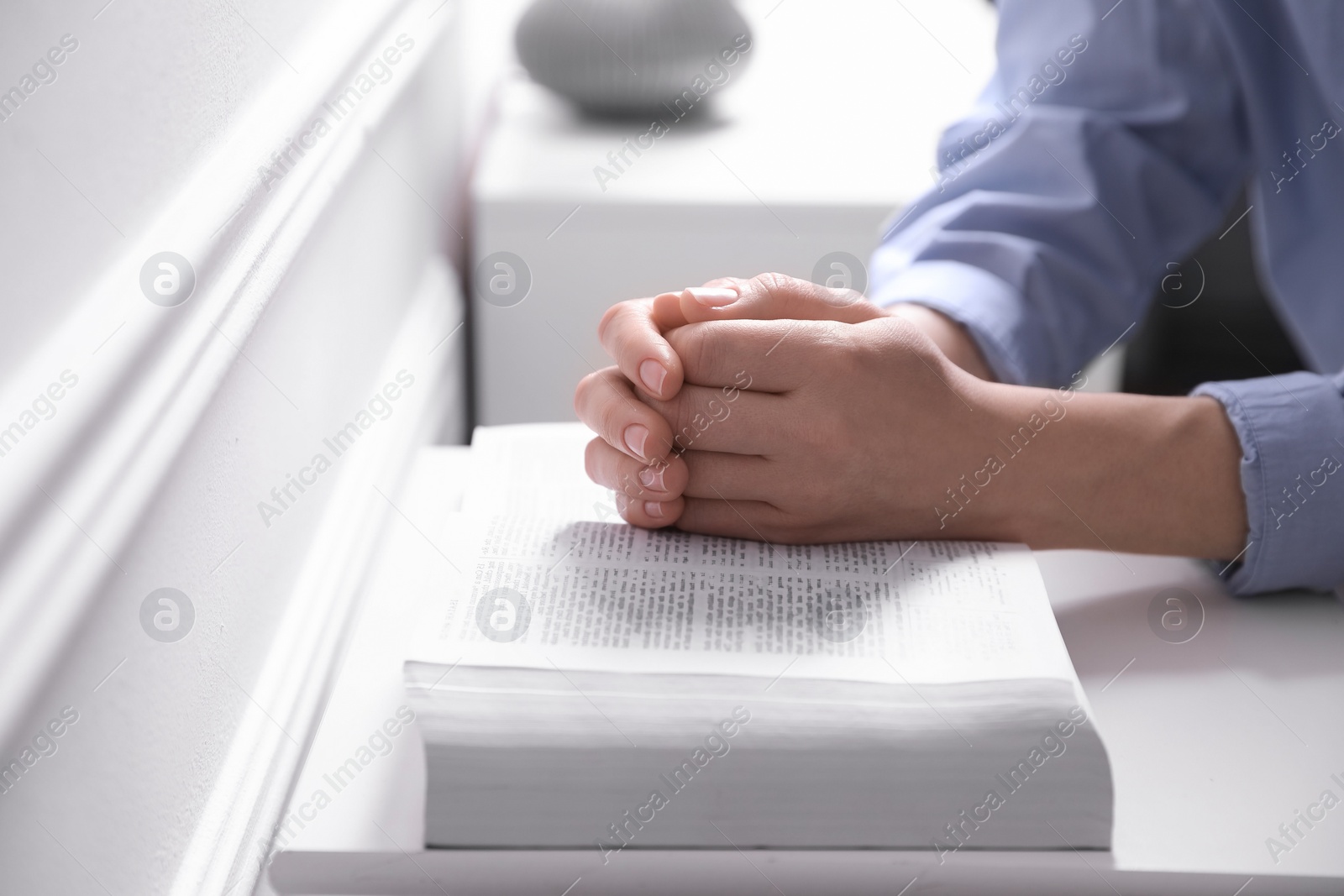 Photo of Religion. Christian woman praying over Bible indoors, closeup