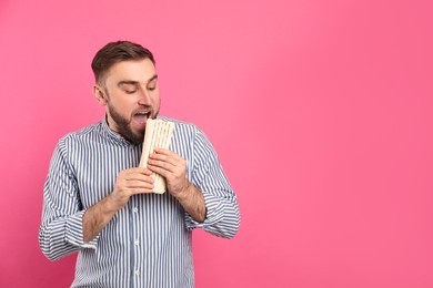 Photo of Young man eating delicious shawarma on pink background, space for text