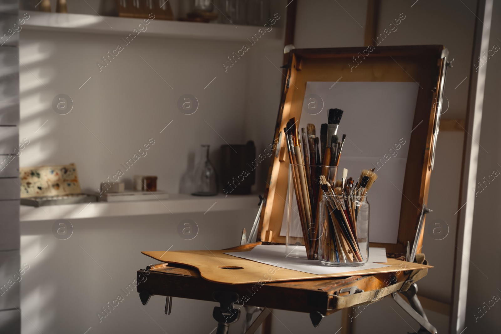 Photo of Holders with different paintbrushes on easel in studio. Artist's workplace