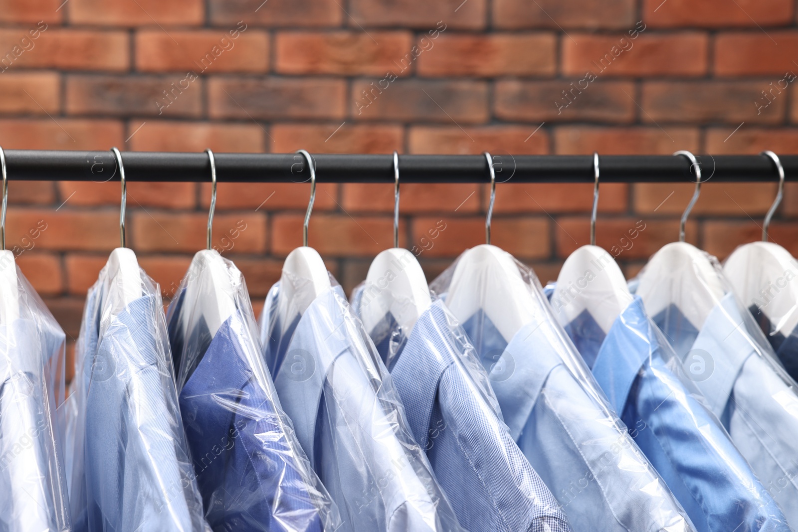 Photo of Dry-cleaning service. Many different clothes hanging on rack against brick wall, closeup