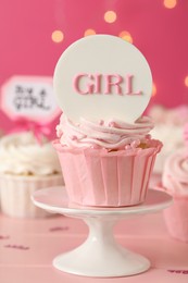 Photo of Beautifully decorated baby shower cupcake for girl with cream and topper on pink wooden table