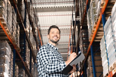 Photo of Happy manager holding clipboard in warehouse with lots of products., low angle view