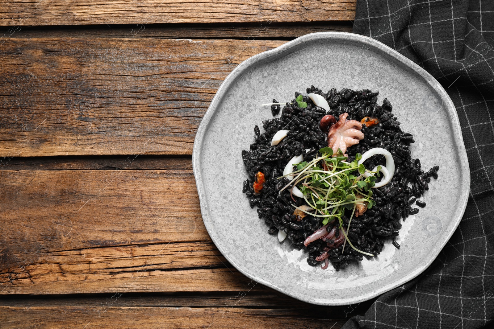 Photo of Delicious black risotto with seafood on wooden table, top view