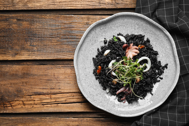Delicious black risotto with seafood on wooden table, top view