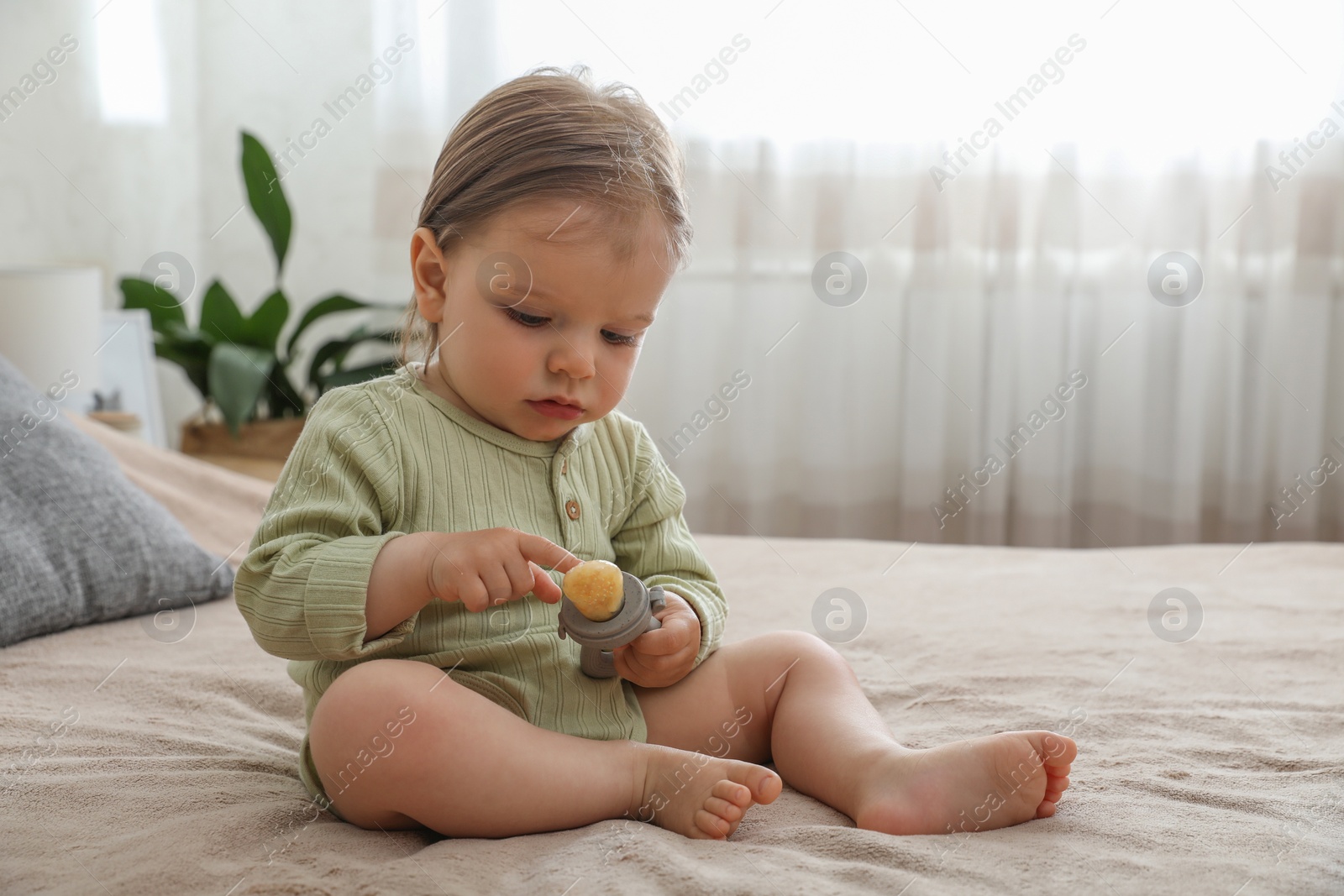 Photo of Cute baby girl with nibbler on bed at home. Space for text