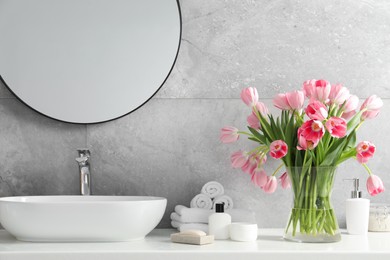 Photo of Vase with beautiful pink tulips and toiletries near sink in bathroom