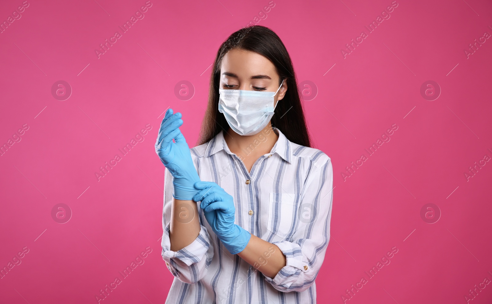 Photo of Woman in protective face mask putting on medical gloves against pink background