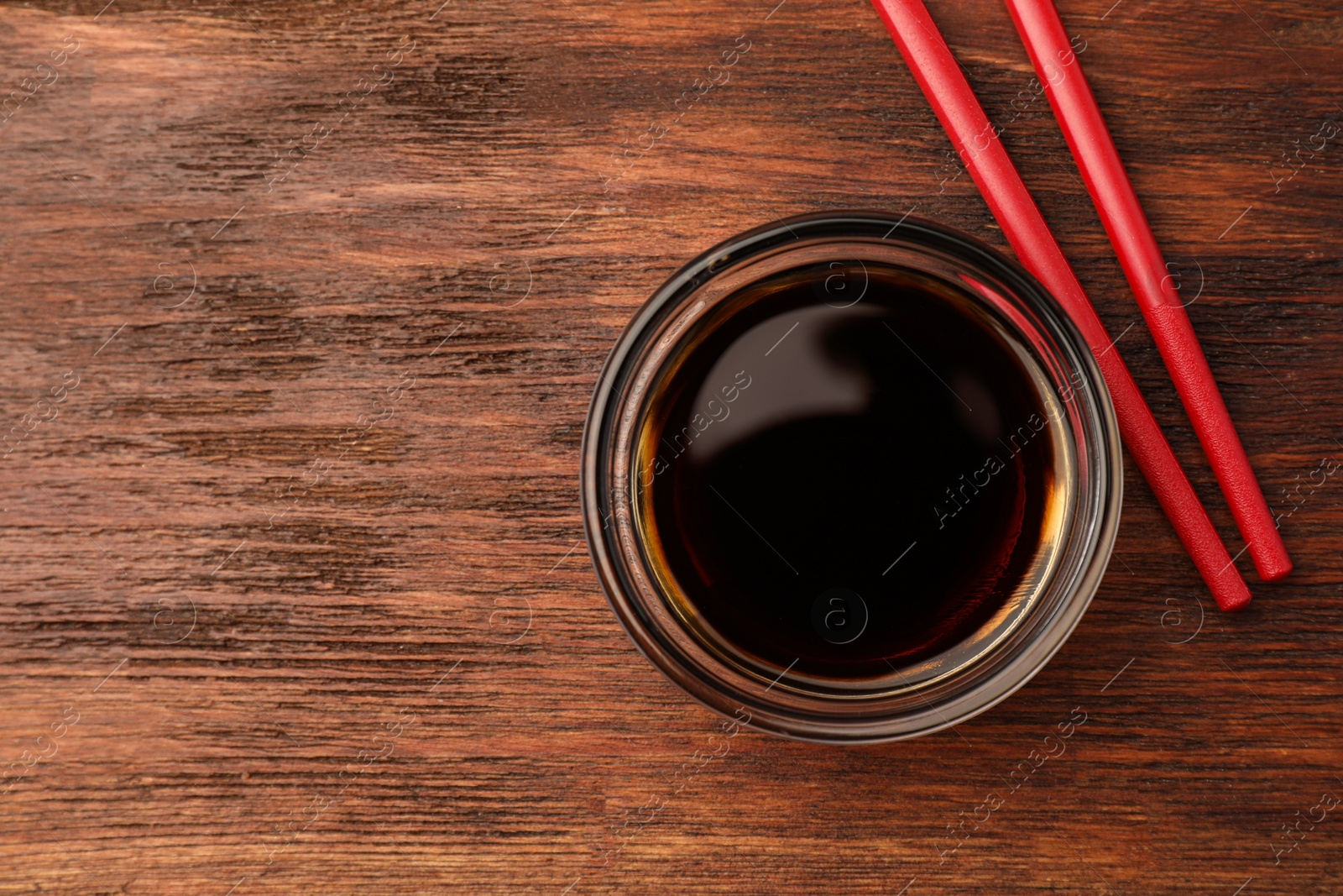 Photo of Bowl with soy sauce and chopsticks on wooden table, top view. Space for text
