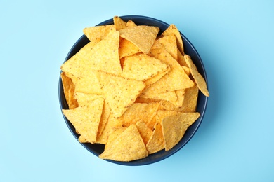 Bowl of tasty Mexican nachos chips on light blue background, top view