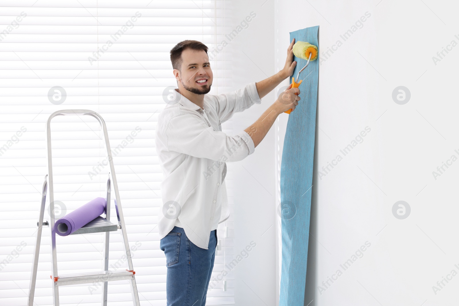 Photo of Man hanging light blue wallpaper in room