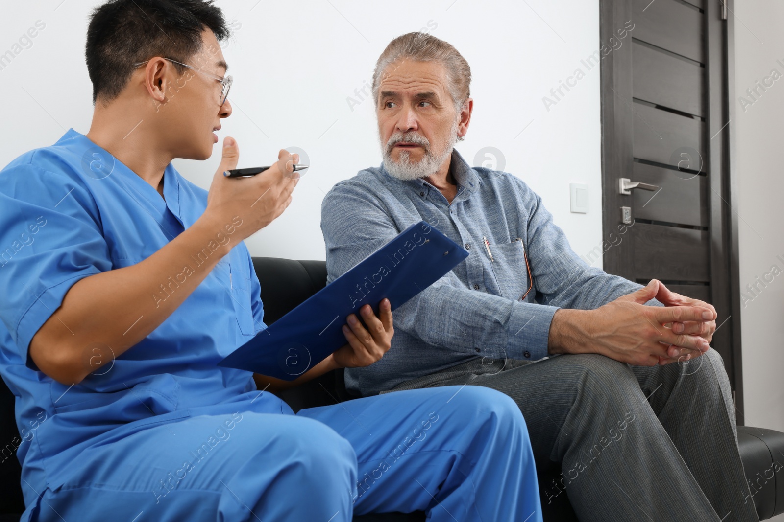 Photo of Doctor with clipboard consulting senior patient in clinic