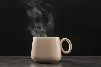 Photo of Steaming ceramic cup on grey table against dark background