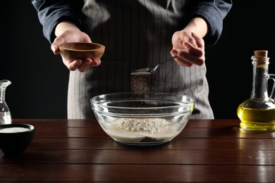 Photo of Making bread. Woman putting dry yeast into bowl at wooden table, closeup