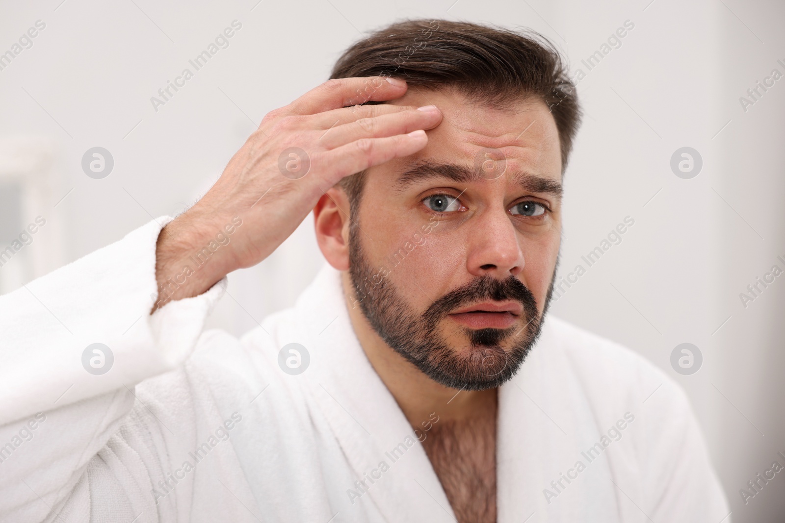 Photo of Skin problem. Confused man touching his face indoors