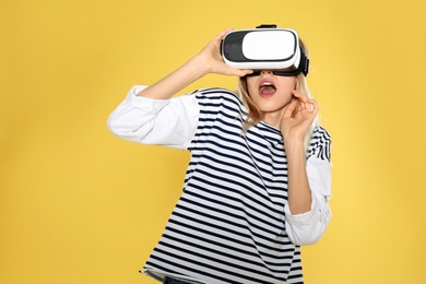 Emotional woman playing video games with virtual reality headset on color background