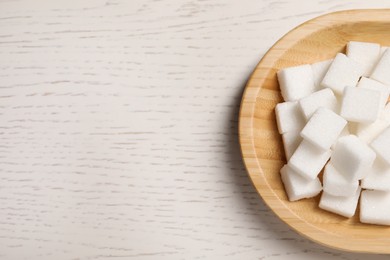 Photo of Refined sugar cubes in bowl on white wooden table, above view. Space for text