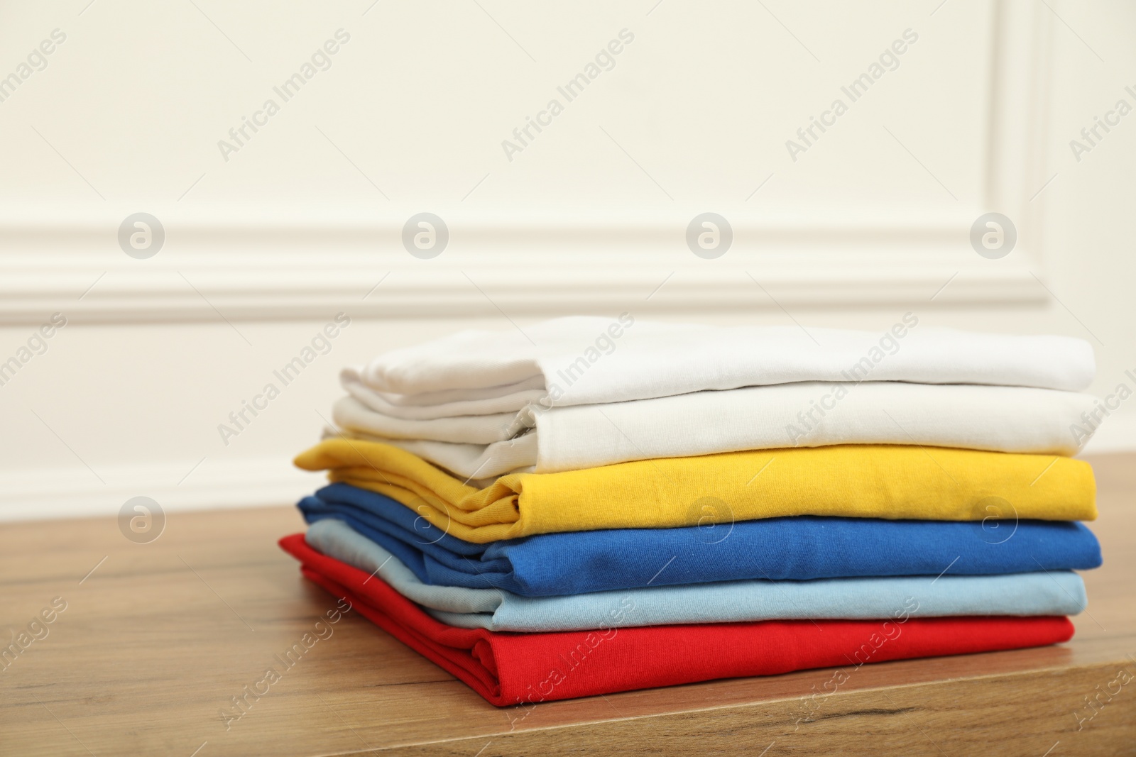 Photo of Sorting and organizing. Stack of different folded clothes on wooden table near white wall, space for text