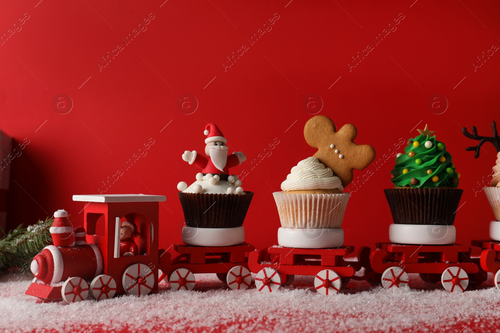 Photo of Toy train with tasty Christmas cupcakes on red background